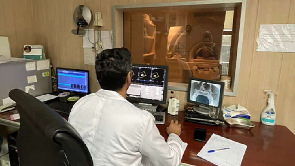 تصویری از اپراتور پشت سیستم در حال بررسی وضعیت ام ار آی بیماری که در داخل دستگاه است 